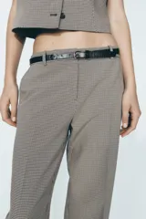 Pantalón de tiro alto con estampado a cuadros en tonos beige y marrón, con bolsillos delanteros y falsos bolsillos traseros. Incluye cinturón marrón con hebilla metálica.