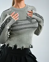 Sweater gris de punto con rayas verticales negras, cuello redondo, mangas largas con detalle de flecos y ruedo con terminación irregular.