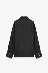 Camisa amplia color negro confeccionada con hilatura de lino. Tiene cuello solapa, manga larga, bolsillo de plastrón en el delantero, bajo asimétrico y cierre frontal con botones.