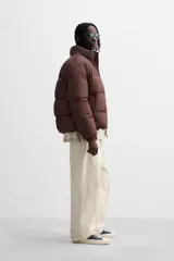 Campera puffer marrón con cuello alto, cierre frontal con cremallera, bolsillos laterales y puños elásticos.