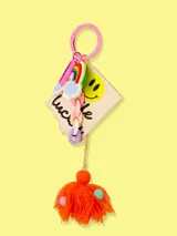 Llavero con aro rosado y dijes colgantes: arcoíris, nube, lápiz labial, smiley face, cadena de eslabones y borla de hilo naranja con lunares de colores.