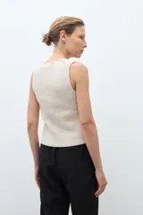 Chaleco de punto color beige melange, con escote en V y cierre frontal de dos botones oscuros. Es sin mangas y de corte ajustado.