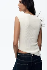 Top color crema de cuello redondo y sin mangas. Presenta detalle de drapeado lateral y bajo asimétrico.