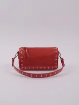 Bandolera color rojo de cuero con tachas plateadas. Tiene dos asas desmontables, una corta con tachas para llevarla en la mano o al hombro y una larga para llevarla al hombro o cruzada. Tiene bolsillo interior con cierre y forro.