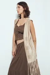 Chaleco largo color beige claro, estilo chaleco de gamuza, con apliques metálicos circulares perforados y largos flecos en el ruedo.