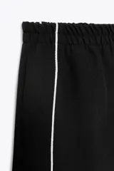 Pantalón negro capri de tiro alto con bolsillos delanteros, cintura elástica y banda lateral blanca a contraste.