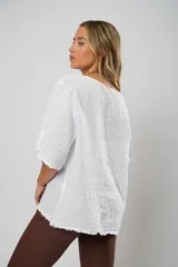 Blusa blanca de lino con corte asimétrico, mangas 3/4 con botones y cuello redondo amplio.