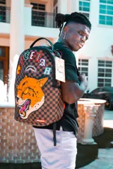 Mochila Sprayground en colaboración con el jugador de la NFL Tyreek Hill. Diseño con estampado a cuadros en tonos marrones y aplique de la cara de un guepardo.