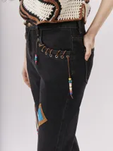 Pantalón de jean azul con parches de colores, tiro alto, corte mom-fit, apliques de cuero trenzado alrededor de los bolsillos frontales y canutillos en la parte frontal.