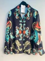 Camisa holgada estampada con diseño paisley en tonos azul, naranja y beige. Tiene cuello solapa, cierre abotonado y mangas largas. Corte clásico.