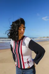 Sweater tejido a mano en algodón reciclado, color blanco con detalles en azul marino y rojo. Presenta cuello redondo, mangas largas en color azul marino y un diseño de brújula bordada en el frente.