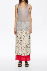 Falda midi de corte línea A, con estampado moteado en tonos beige y marrón oscuro. Presenta un forro rojo que asoma en el bajo y una capa superior de tejido ligero con un patrón similar al moteado.