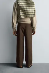 Pantalón relaxed fit color marrón confeccionado en tejido de algodón con estructura twill. Cintura con pliegues frontales, bolsillos laterales en cadera y detalle de bolsillos traseros de doble vivo con botón. Cierre frontal con cremallera y botón.