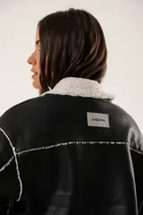 Campera corta negra de cuero sintético con cuello y forro de piel sintética blanca.