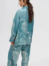 Camisa oversize celeste con estampado tie-dye, bolsillo en el pecho con logo bordado y botones marrones.