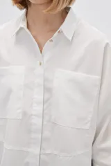 Camisa color verde claro, de corte holgado, con cuello clásico, cierre frontal con botones, mangas 3/4 y dos bolsillos de parche en el pecho.