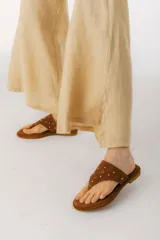 Sandalias chatitas color beige con tira de cuero en forma de T y apliques de tachas doradas.