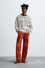Camiseta relaxed fit de manga larga confeccionada en tejido compacto de algodón a rayas horizontales blancas y negras. Tiene cuello redondo y detalle de estampado de flores rojas en el bajo. Edición especial Zara x Otis Kwame Kye Quaicoe.