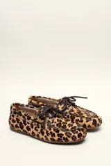 Mocasín tipo boat shoe con estampado de vaca en tonos marrón y blanco, confeccionado en cuero. Cuenta con cordones de cuero marrón oscuro y suela de goma.