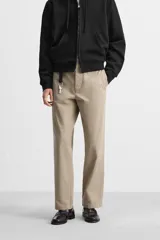 Pantalón chino color verde militar, de corte recto, con bolsillos laterales y traseros de vivo. Cierre frontal con cremallera y botón.