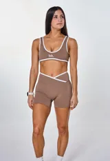 Conjunto deportivo color marrón con detalles en blanco, compuesto por un top con logo "bk." y unos shorts de tiro alto.