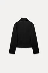 Chaqueta corta negra de cuello solapa y manga larga con puños. Tiene bolsillos de parche en el frente y cierre frontal con botones.