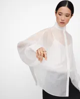 Camisa blanca de manga larga, con cuello chimenea alto y botonadura frontal oculta. El tejido es semitransparente y presenta una textura ligera.