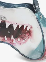 Bolso de hombro con forma estructurada y asimétrica, estampado con la boca abierta de un tiburón en tonos blancos, rojos y azules. Posee un asa ajustable y un pequeño logo metálico frontal.