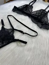Conjunto de lencería negro de encaje, compuesto por un corpiño tipo bralette, una tanga de tira doble regulable, un portaligas desmontable y ligas regulables.