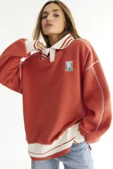 Buzo celeste con cuello polo y puños en rib color verde lima. Tiene un parche con el logo de la marca en el pecho y rayas horizontales en el ruedo.