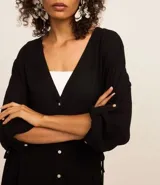 Salida de playa tipo bata color blanco, con textura maquinetada, cuello V, mangas 3/4 con detalle de botón, cierre por botones y reguladores laterales con cordón.