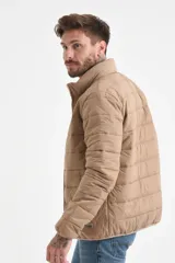 Campera acolchada color beige, con cuello alto y cierre frontal. Presenta costuras horizontales que crean el efecto capitoné.