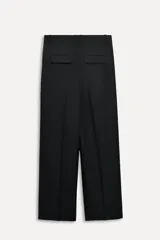 Pantalón negro de tiro medio con cintura con trabillas, bolsillos laterales y con solapa en espalda. Detalle de pinzas y raya planchada en delantero. Cierre frontal con cremallera, botón y ganchos metálicos.