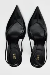 Zapato destalonado negro acharolado con tacón fino y punta. Tiene una tira trasera con elástico.