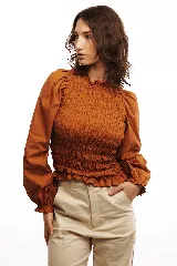 Blusa blanca de algodón con frunces tipo smock en el cuerpo, cuello redondo y mangas largas abullonadas con puños elásticos.