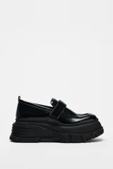Zapato tipo mocasín negro con plataforma y suela track. Presenta tira ajustable adherente y tirador trasero.