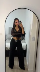 Pantalón de jean negro de tiro alto y corte palazzo, con cinto de cuero negro con hebilla plateada. Blusa de encaje negra con mangas acampanadas.