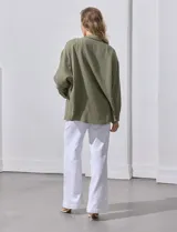Camisa blanca de algodón con textura arrugada, cuello con solapa, abertura central con botones y bolsillo aplicado en el pecho. Mangas largas con largo regulable mediante presilla y botón.