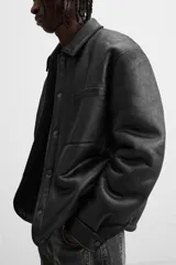 Sobrecamisa marrón de efecto piel con interior de borreguillo combinado a tono, de corte relaxed fit, cuello solapa, manga larga con puños abotonados, bolsillos de plastrón en pecho y laterales en cadera, efecto lavado y cierre frontal con botones a presión.