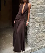 Vestido largo color marrón chocolate, con escote halter profundo y drapeado en el busto. La cintura es ajustada con frunces y un lazo anudado, y la falda es fluida con una abertura lateral.
