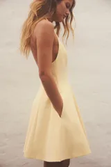 Vestido corto amarillo con cuello halter y espalda descubierta. Falda con vuelo y cierre trasero con cremallera oculta y botones ocultos en el cuello.