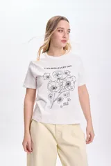 Remera blanca de algodón con cuello redondo y mangas cortas. Estampa de flores y texto en color negro.