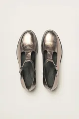 Zapato guillermina color bronce con acabado metalizado, con correa sobre el empeine con hebilla ajustable y suela de goma negra con plataforma.