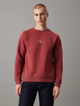Buzo de felpa color ladrillo con cuello redondo, puños y bajo acanalados. Presenta un logo bordado de Calvin Klein Jeans en el pecho.