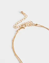Collar corto dorado de doble cadena, con dije de relicario en forma de corazón con flores rosadas.