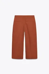 Pantalón marrón de tiro alto, corte ancho y largo midi. Presenta pinzas delanteras, bolsillos laterales y traseros de parche. Cierre frontal con cremallera y gancho metálico.