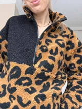 Sweater de peluche con cierre de media cremallera, mitad negro liso y mitad con estampado animal print en tonos marrones y negros.