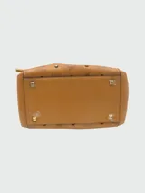 Cartera bombonera de cuero color camel con monograma estampado y tachas doradas.