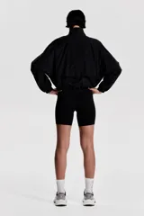 Campera negra de nylon repelente al agua y rompevientos con cuello elevado, cierre con protección para el mentón y bolsillos laterales con cierre. Modelo con hombros caídos, orificios de ventilación en las sisas y mangas murciélago con puños elásticos. Panel de ventilación en malla en la parte baja de la espalda y cordón para ajustar elástico con topes en el bajo. Forro de malla.