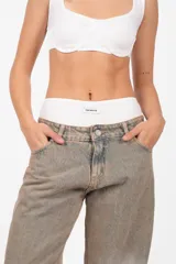 Pantalón de denim corte recto, tiro medio, color arena. Acceso con cierre metálico y botón personalizado. Cintura con cinco presillas, logo estampado en la parte trasera y bolsillos laterales con remaches. Lavado artesanal con matizado color arena. Los tonos pueden variar.